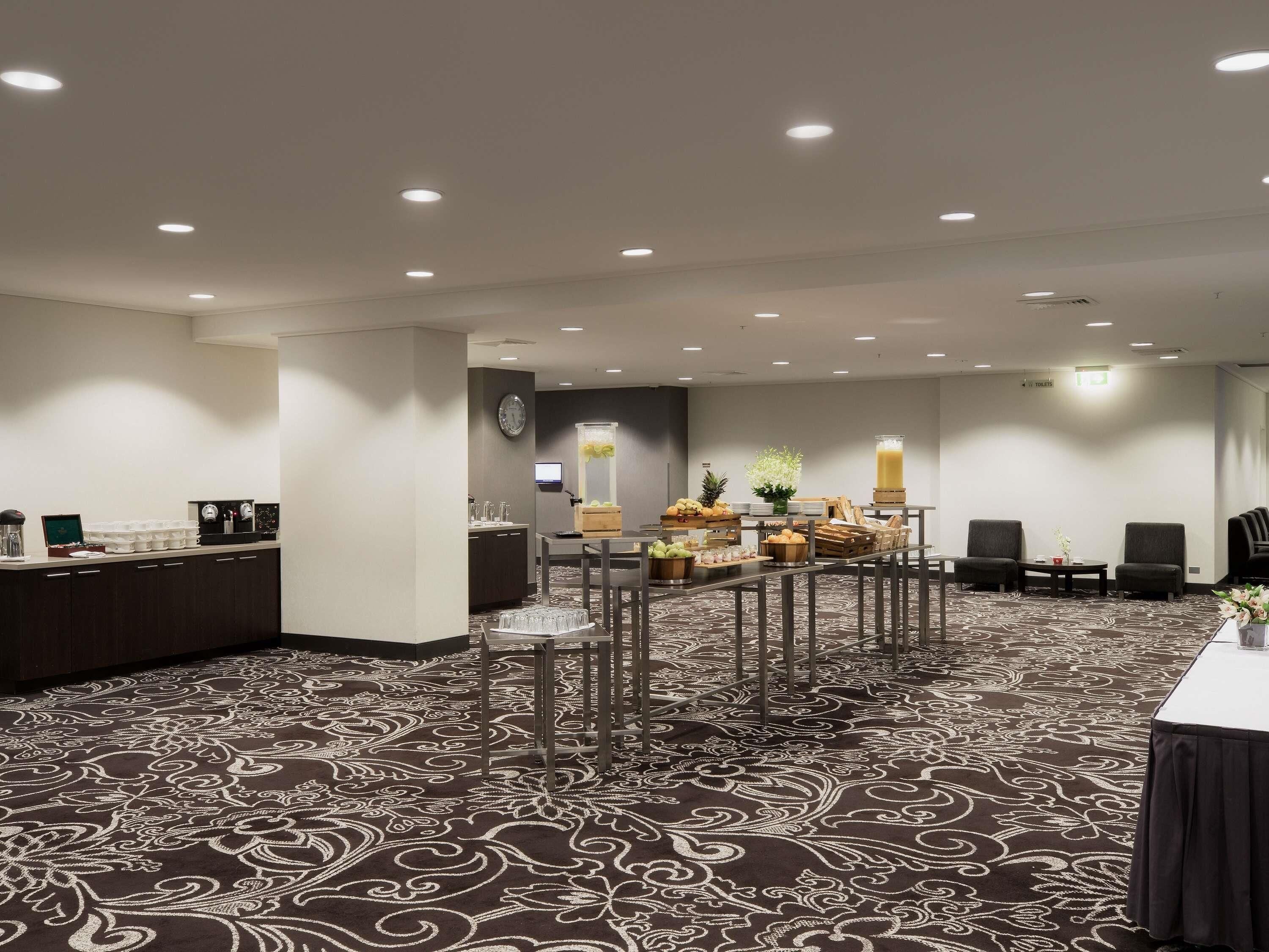 Ein Hotelzimmer mit Essbereich, einem Buffet mit Früchten und Getränken sowie einer Uhr an der Wand.