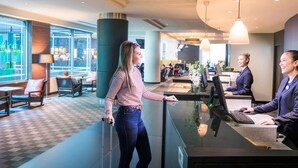 Un moderno vestíbulo de hotel con mostrador de recepción, zona de estar y grandes ventanales con vistas a la ciudad.