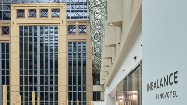 Un moderno vestíbulo de hotel con techo alto, ventanas amplias y una zona de estar con mobiliario de mimbre.