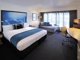 A modern hotel room with a large bed, a sofa, a desk, and a chair.