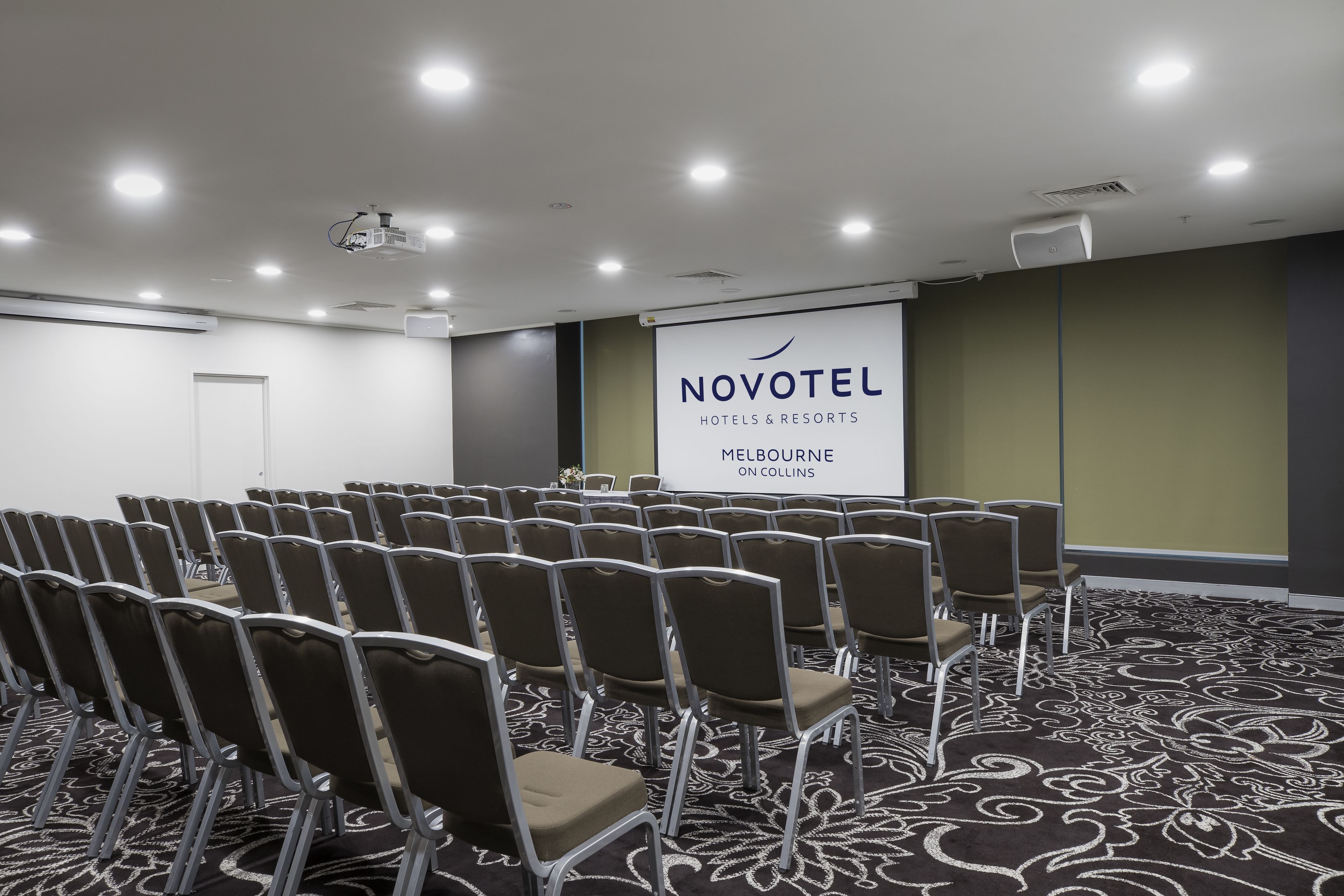 A conference room with rows of chairs, a projector screen, and a carpeted floor.