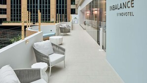 Un pasillo moderno de hotel con mobiliario de mimbre, un muro de cristal y un cartel que dice 'INBALANCE BY NOVOTEL'.