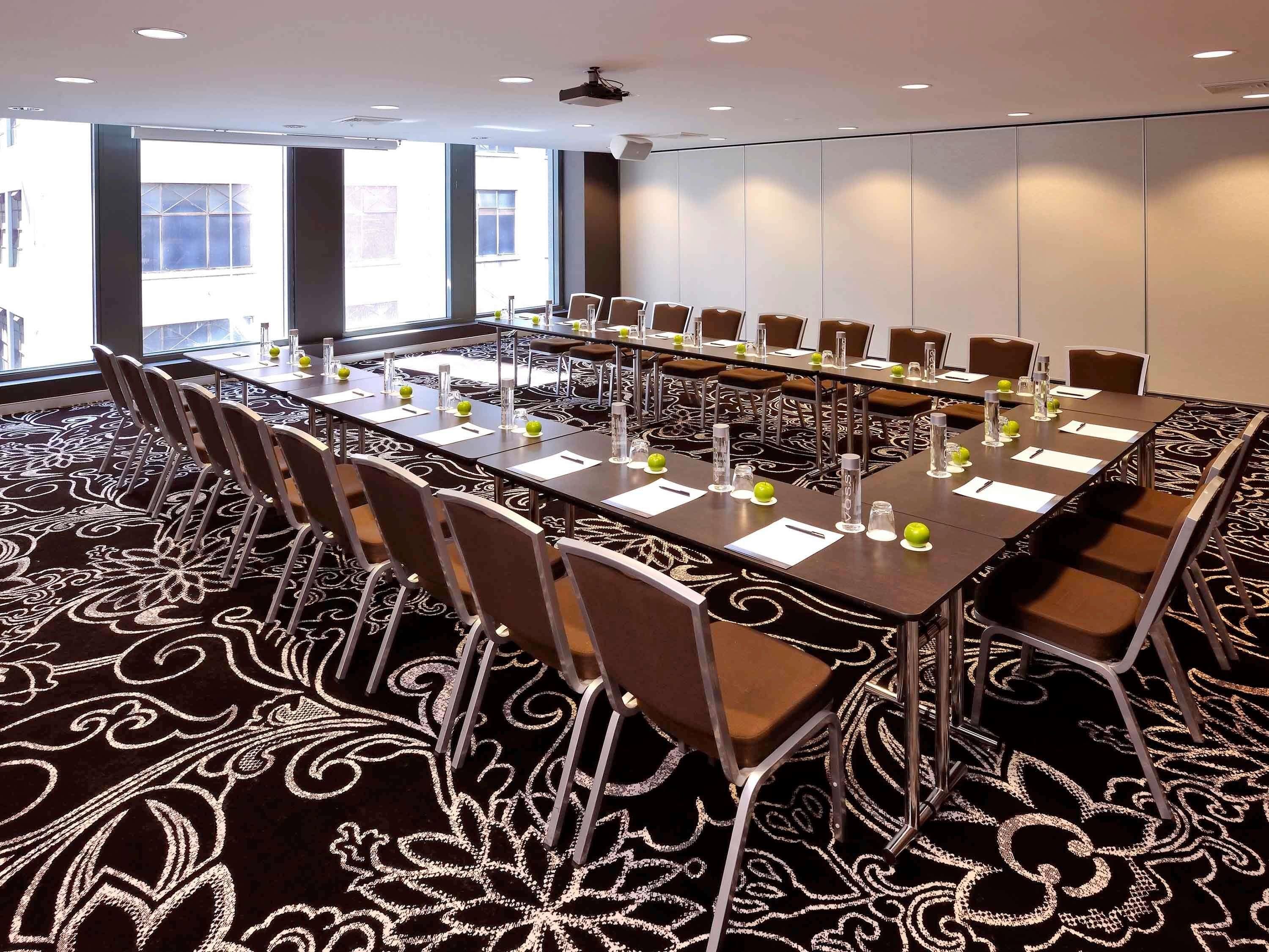 Un salón de conferencias con una mesa larga, sillas y una alfombra estampada.