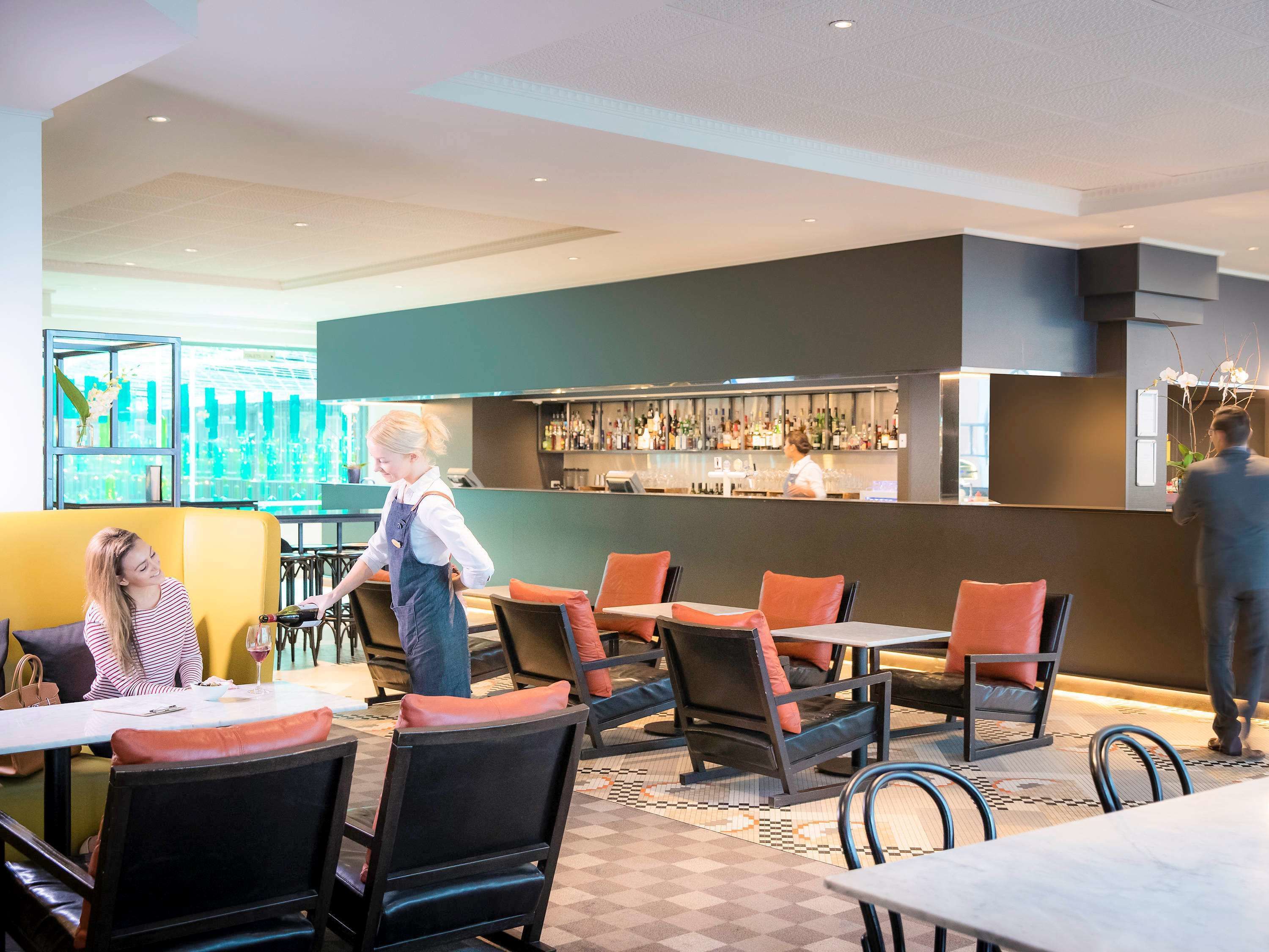Restaurante moderno com área de bar, assentos com almofadas laranja e um bartender atendendo.