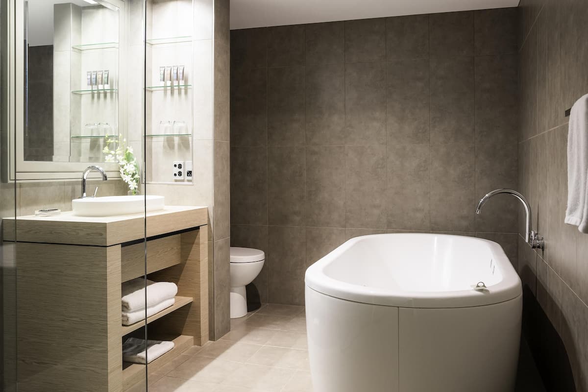 Un baño moderno con una bañera independiente, un tocador con mampara de vidrio y un inodoro.
