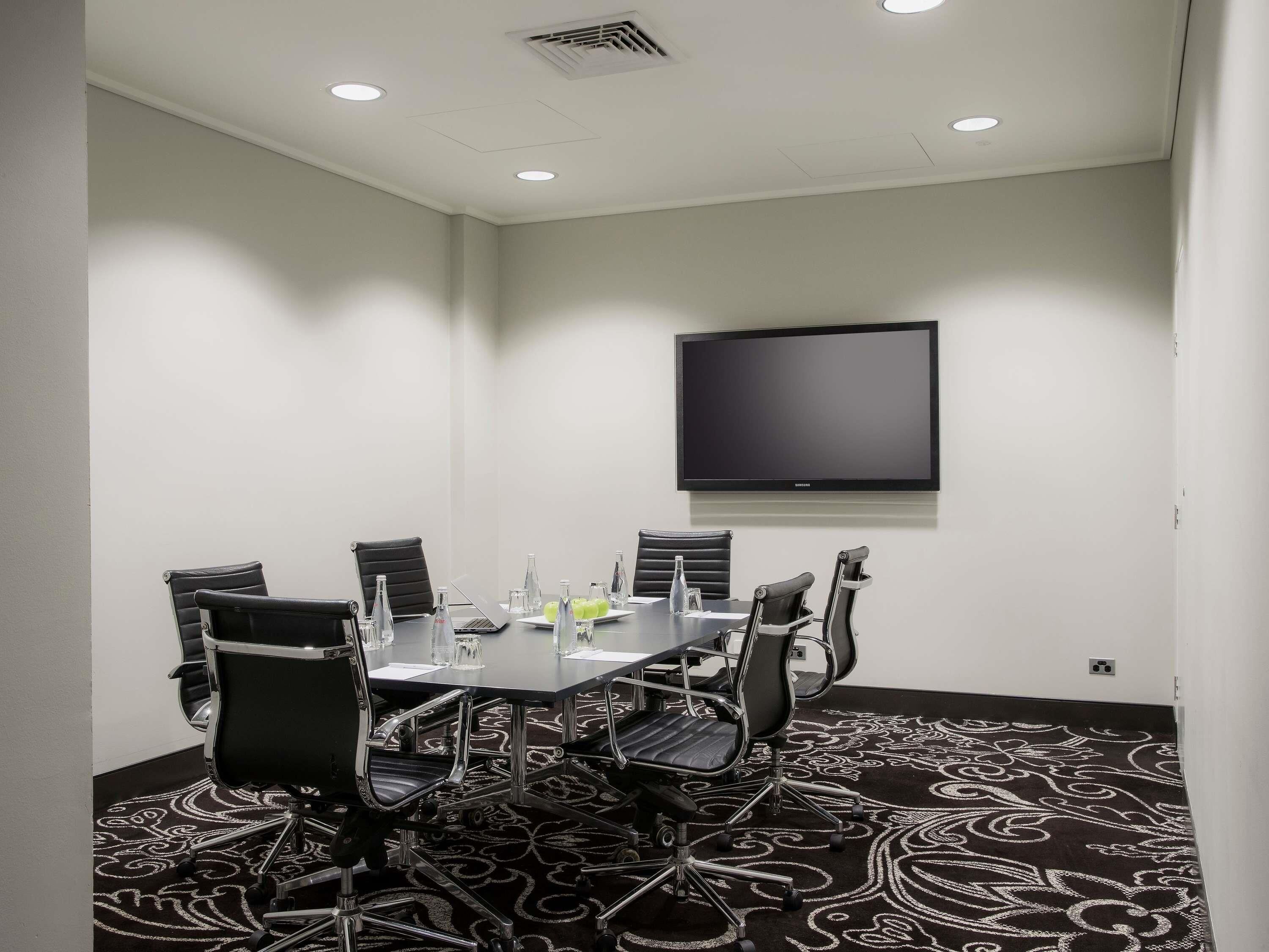 A conference room with a large table, black chairs, a flat-screen TV, and a patterned carpet.