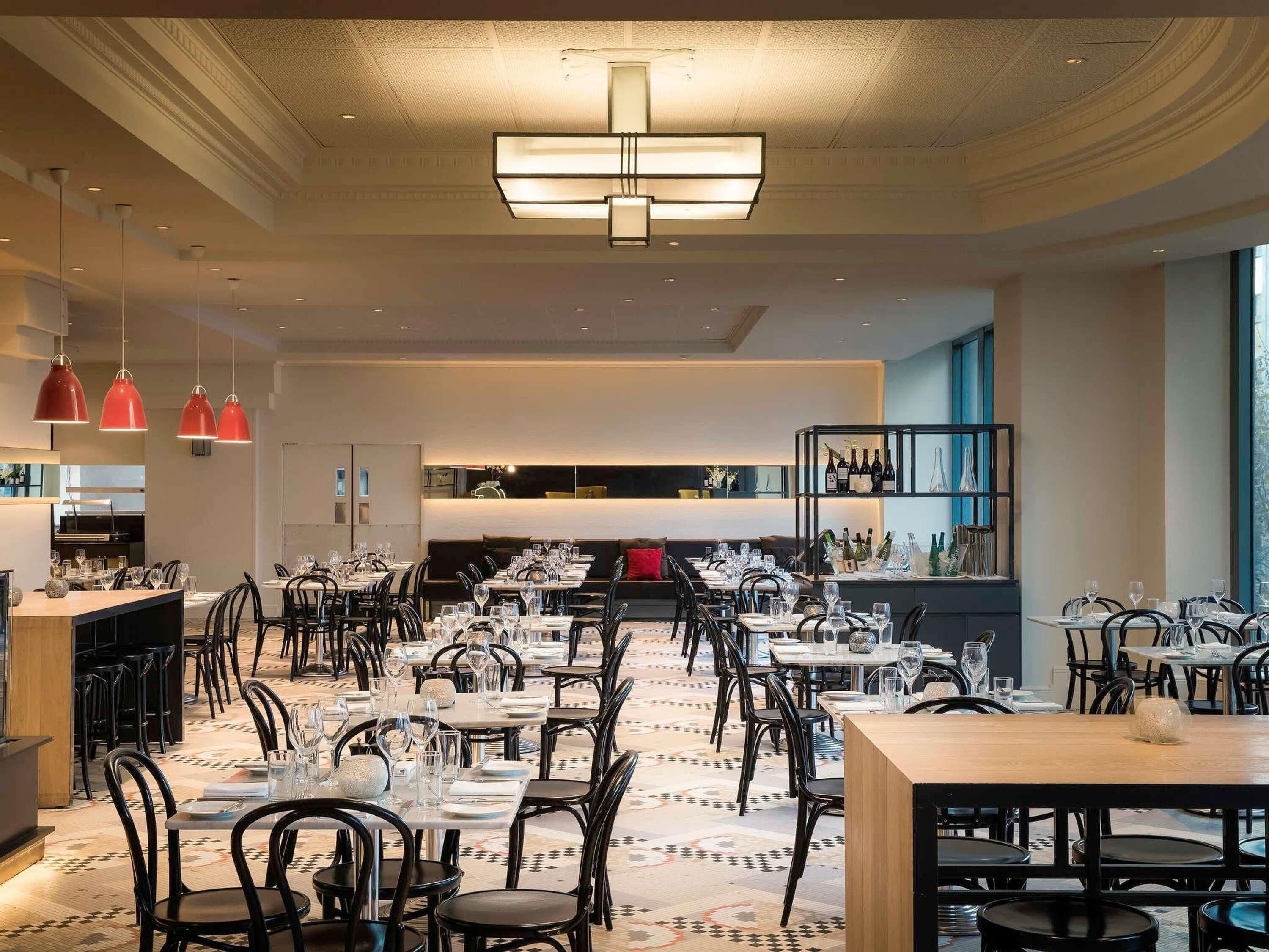 A modern restaurant with multiple dining tables and chairs, a patterned floor, and pendant lighting.