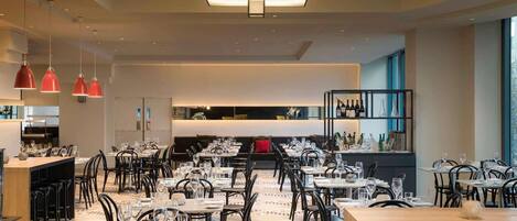 A modern restaurant with multiple dining tables and chairs, a patterned floor, and pendant lighting.