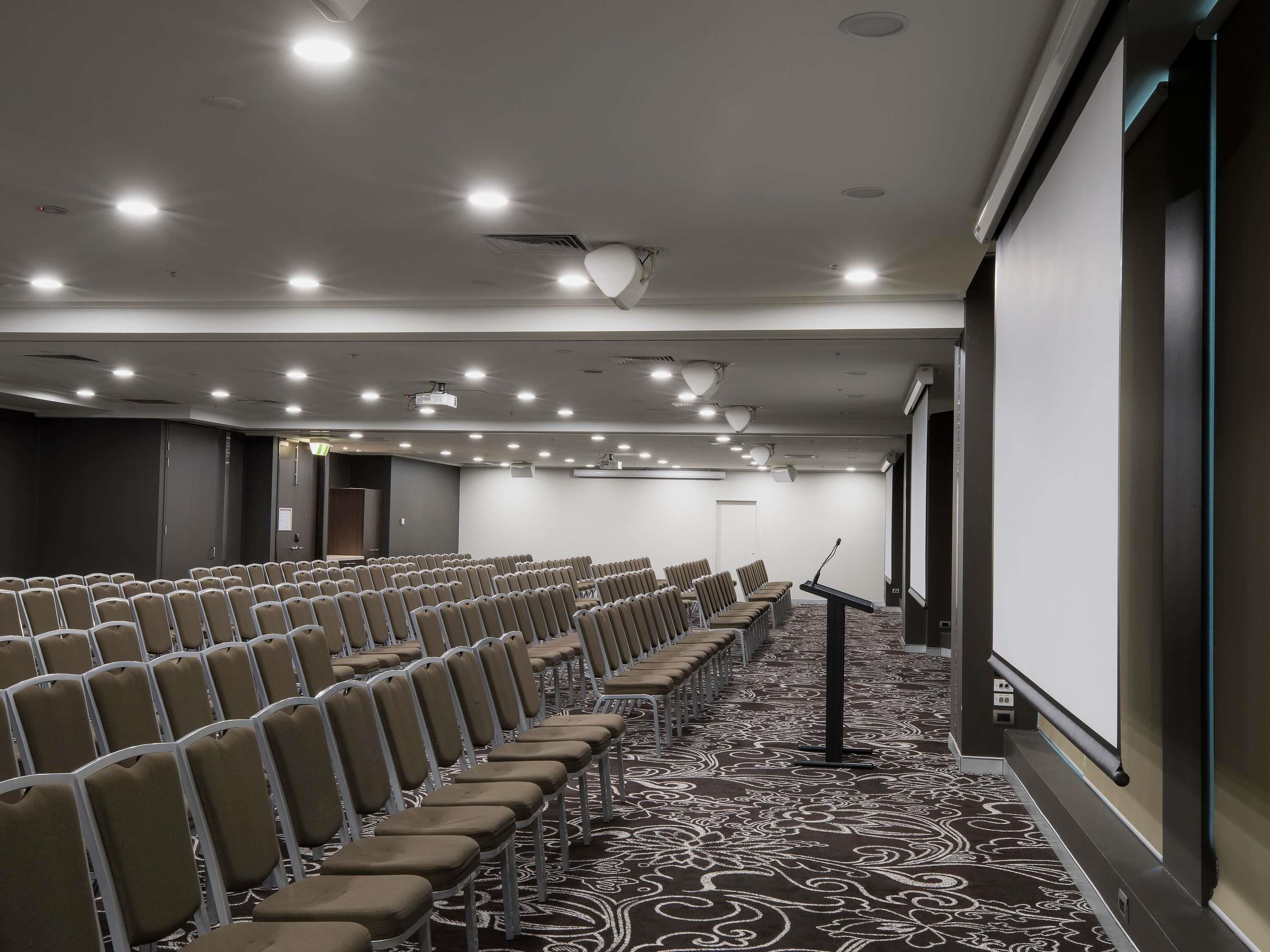 Ein Konferenzraum mit Reihen von Stühlen, einem Projektor und einer Leinwand.