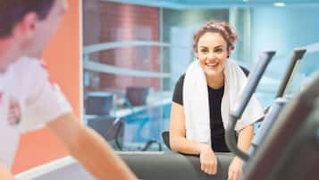 Una persona usando una cinta de correr en un gimnasio con diseño moderno, que incluye paredes de vidrio y una pared azul de acento.