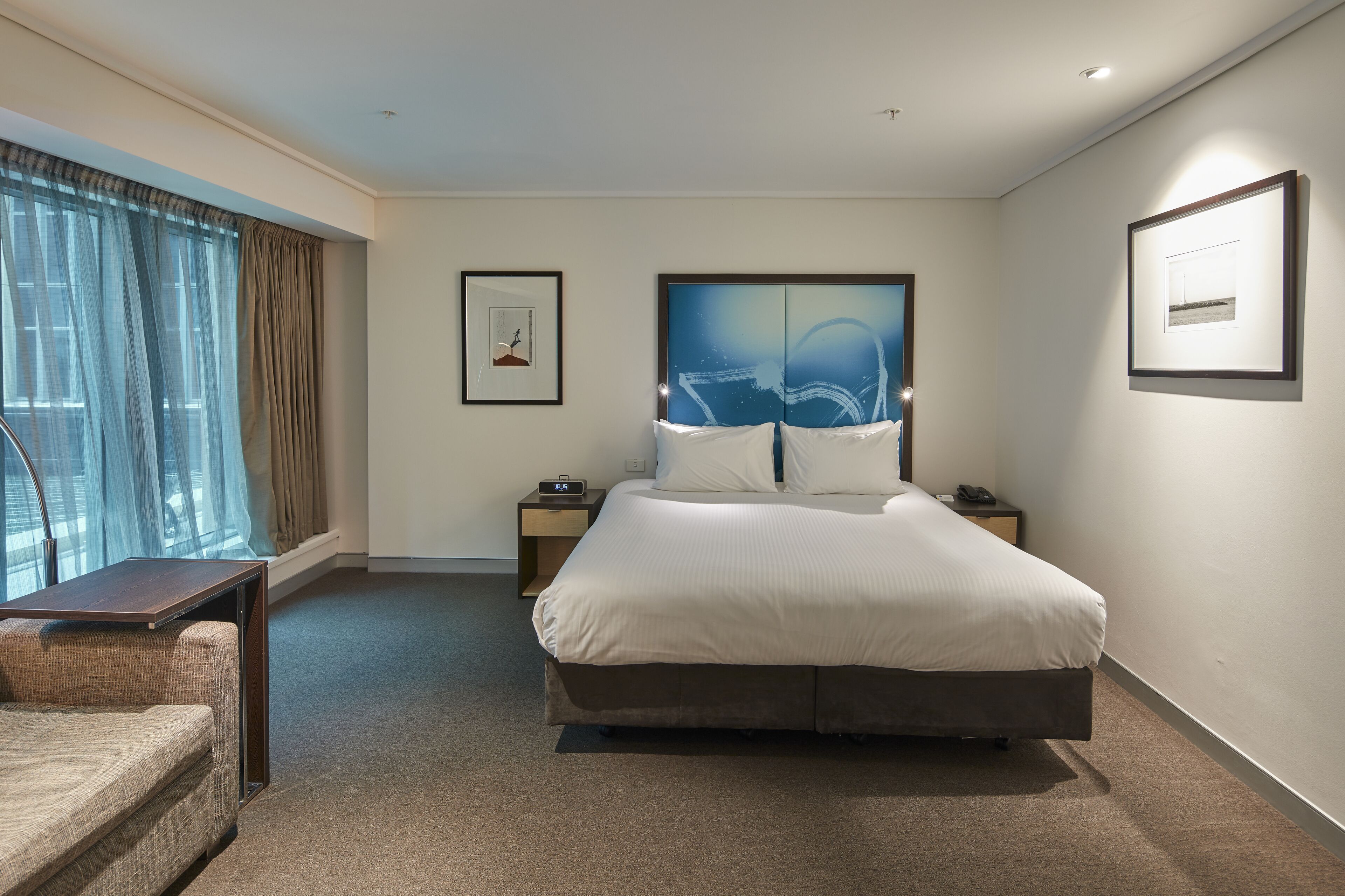 A hotel room with a large bed, a desk, a chair, and a window with curtains.