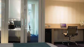 A hotel room with a bed, a desk with a laptop, a chair, and a small table with a vase.