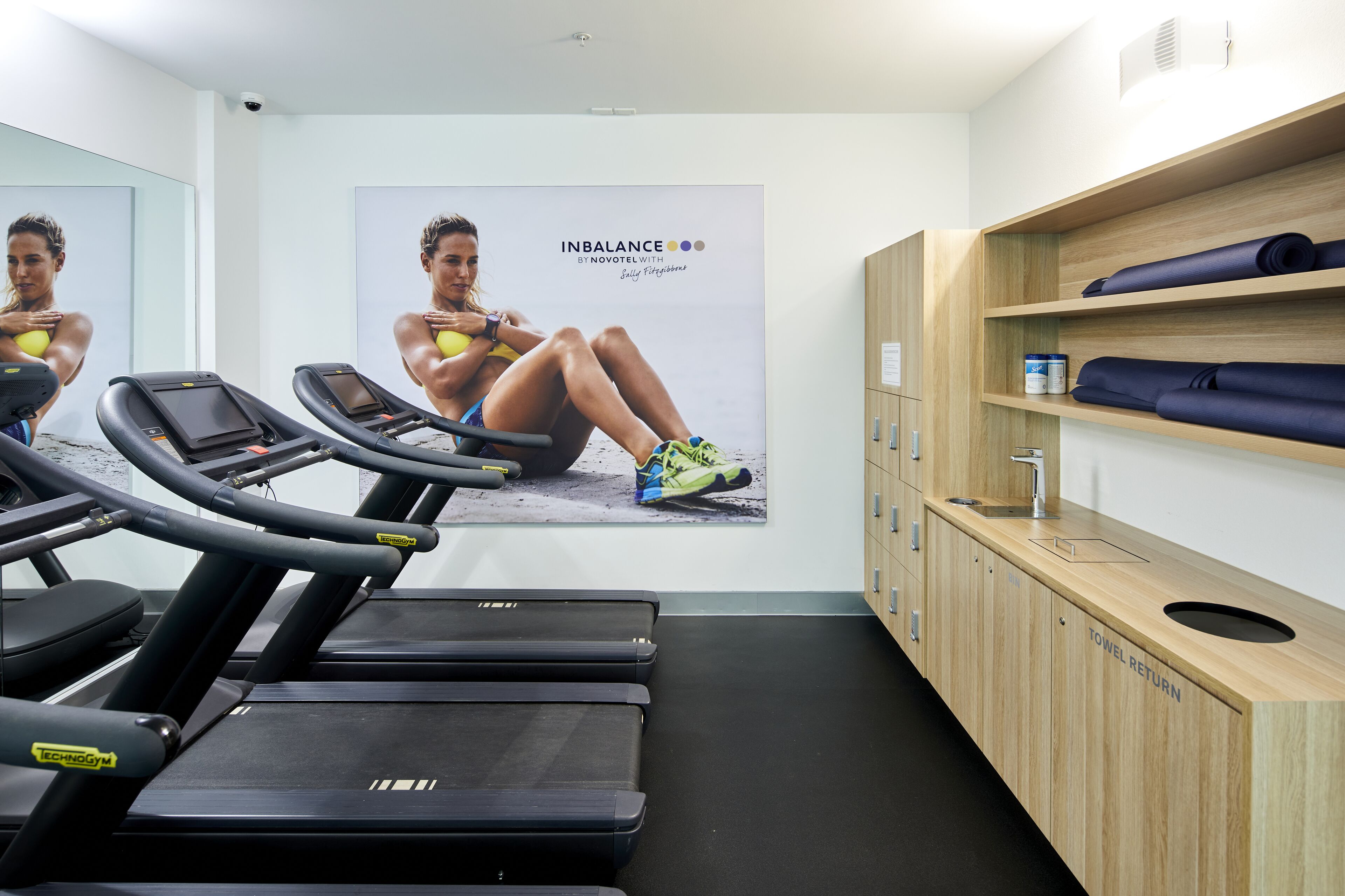 A gym with treadmills, a wall-mounted poster, and a towel return station.