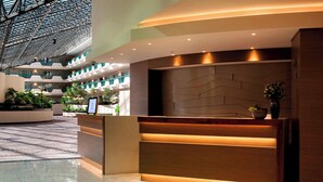 Un hall d’accueil moderne, avec un comptoir en bois, un motif géométrique sur le mur et un vaste atrium agrémenté de balcons et de plantes.