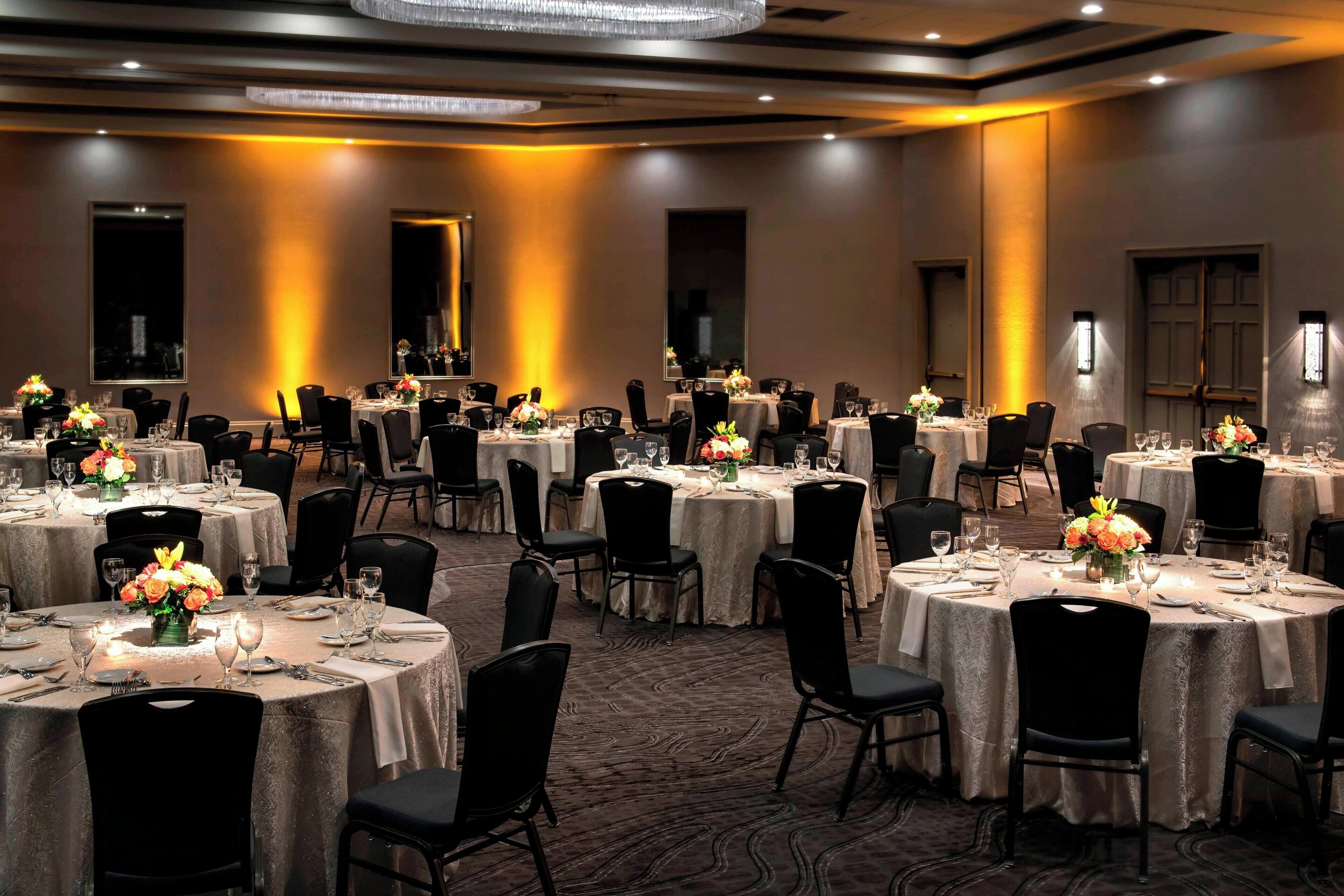A banquet hall with multiple round tables, each set with white tablecloths, black chairs, and floral centerpieces.