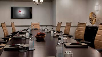 A conference room with a long table, chairs, water bottles, and a television displaying the Marriott logo.