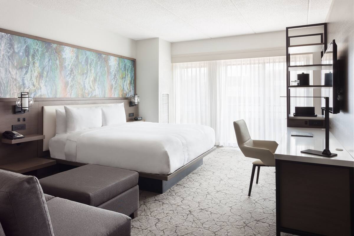 Une chambre d’hôtel moderne dotée d’un grand lit, d’un bureau avec une chaise, d’une télévision et d’un grand tableau abstrait accroché au mur.