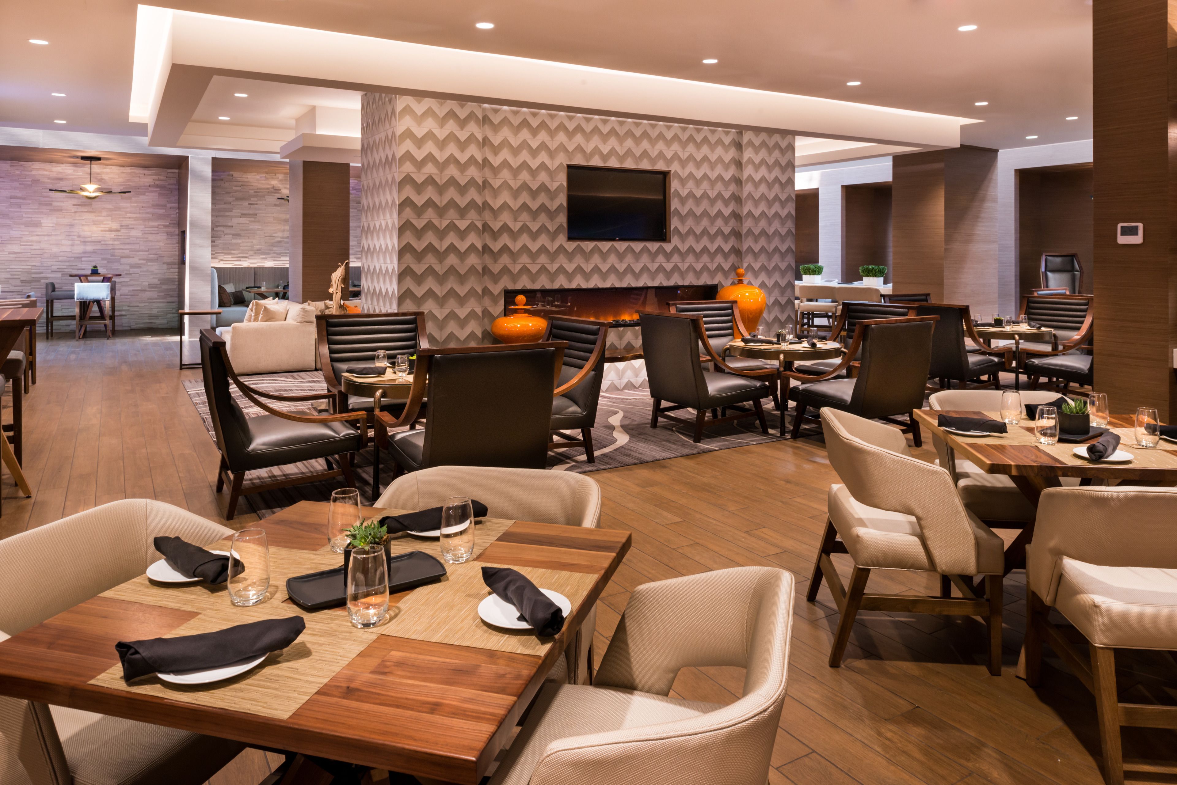 Un restaurante moderno con mesas de madera y sillas de cuero, un televisor de pantalla plana en la pared y un papel tapiz decorativo al fondo.