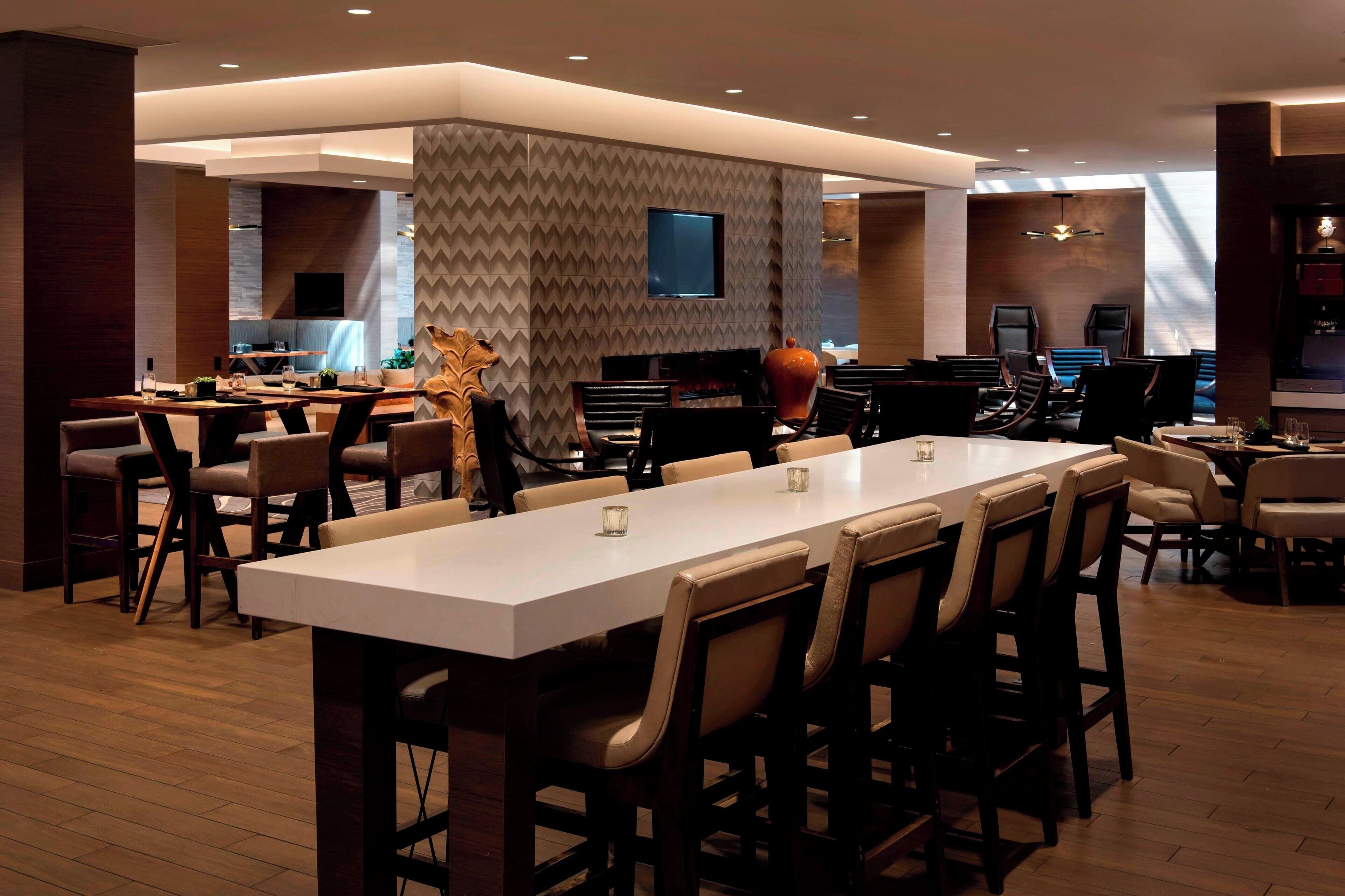 A modern dining area with a long table, multiple chairs, and a television mounted on the wall.