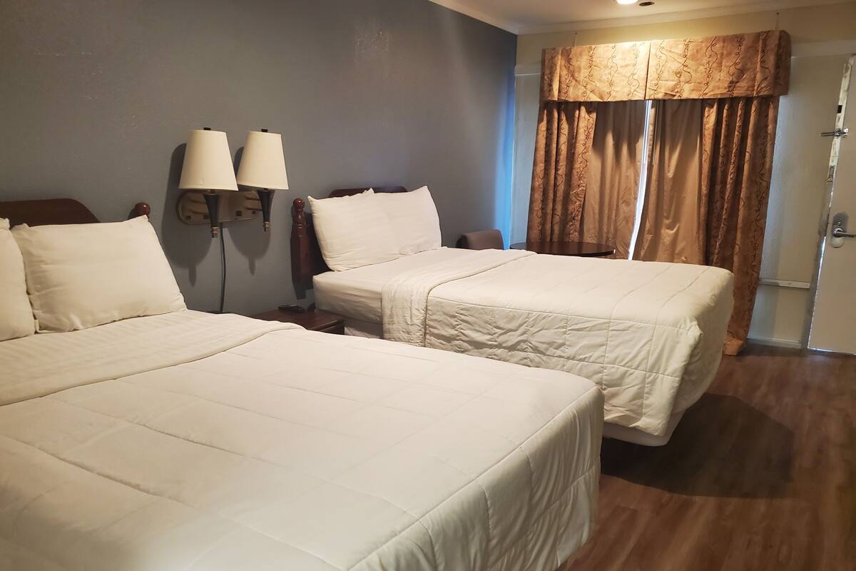 A hotel room with two beds, a nightstand with lamps, a chair, and a window with curtains.