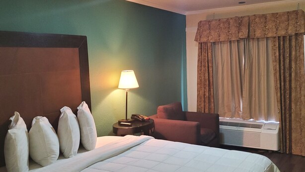 A hotel room with a large bed, a desk with a lamp, a chair, and an air conditioning unit. - Deerfield Inn & Suites (Madison)