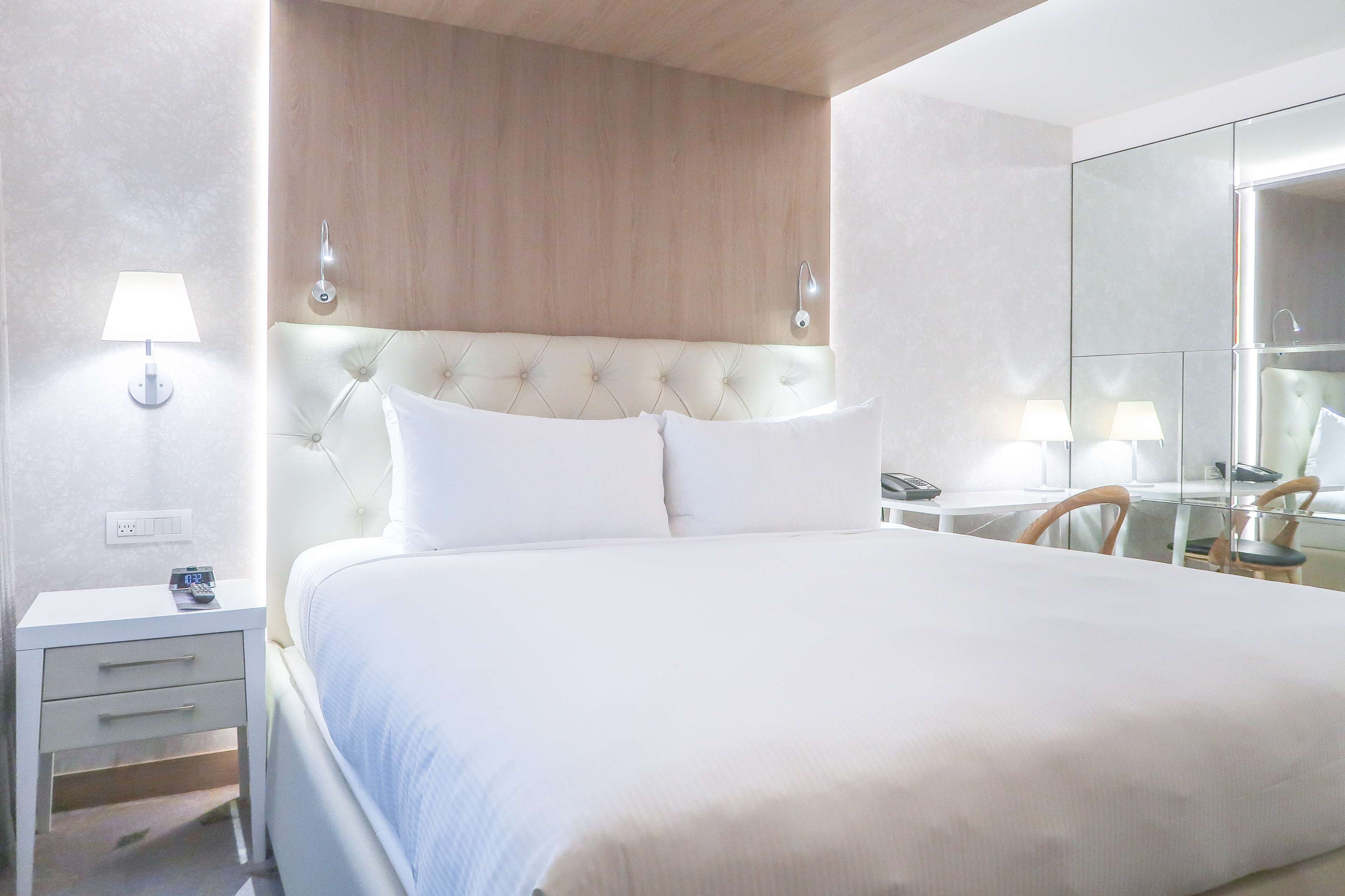 A neatly arranged hotel room with a large bed, bedside tables, a mirror, and a wooden headboard.