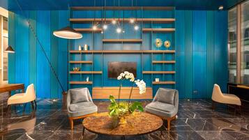 Um hall moderno com parede azul, uma mesa de mármore redonda, duas poltronas cinzas e um arranjo de plantas no centro.