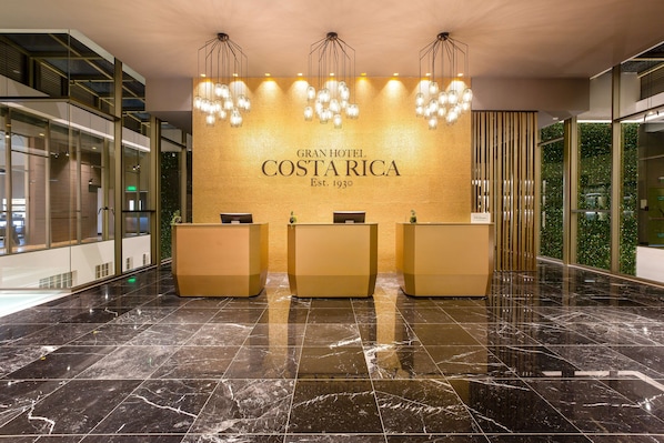 A reception area with a marble floor, three reception desks, and a wall with the hotel's name and establishment year.