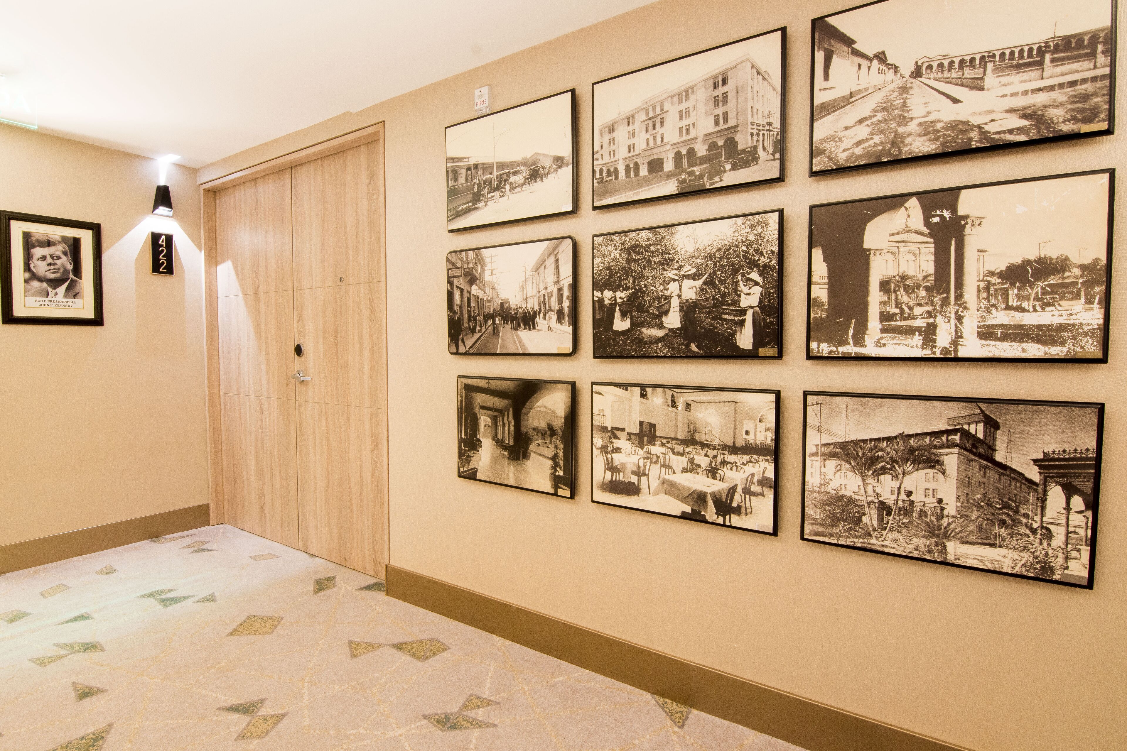 A hallway with a patterned floor, a wooden door, and a series of black and white photographs on the wall.