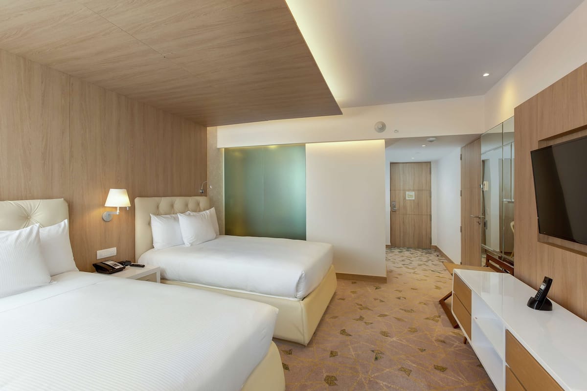 A hotel room with two beds, a TV, a desk, and a bathroom visible through an open door.