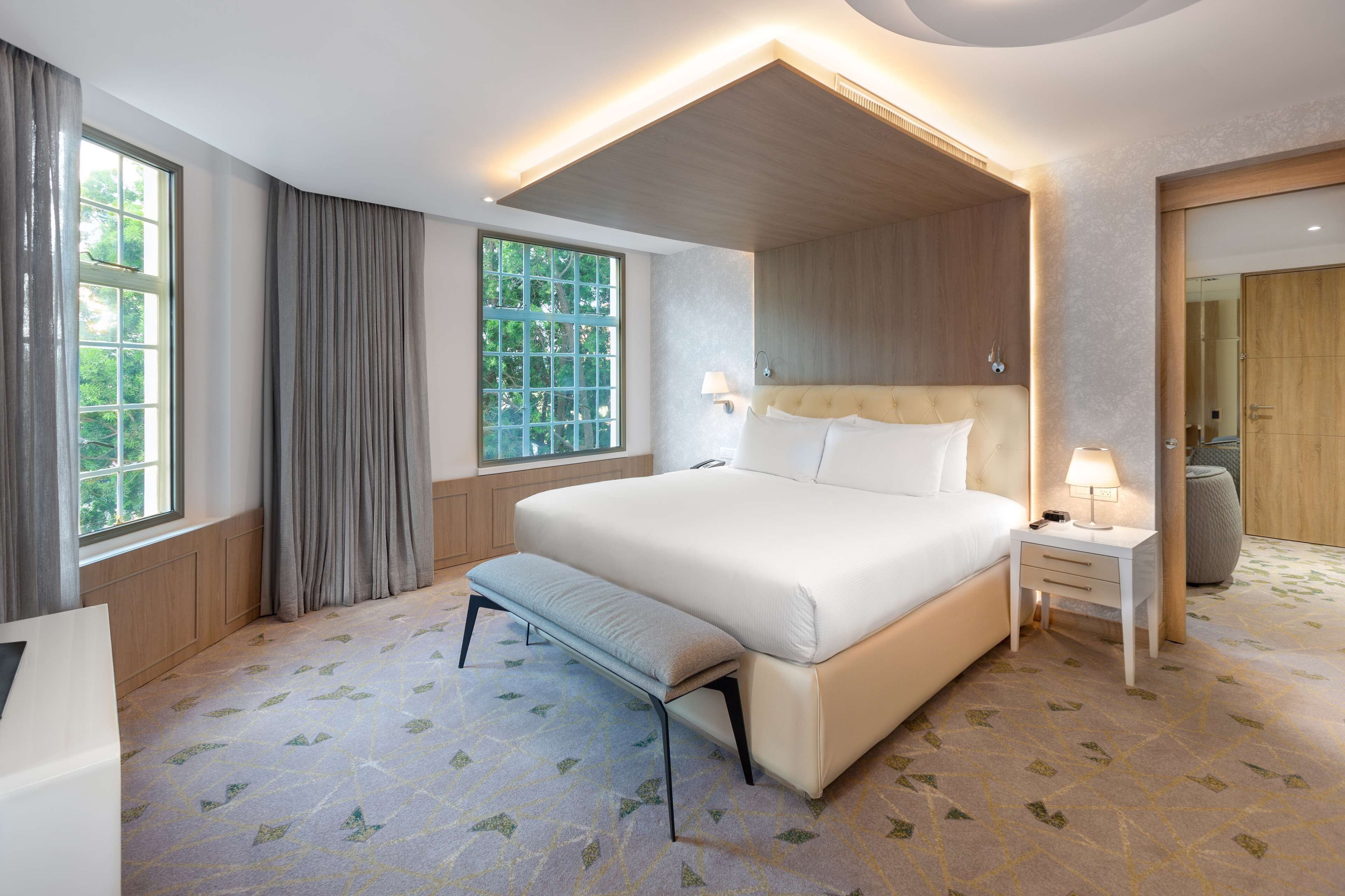 Una camera d'albergo moderna con un letto grande, una panca, un comodino e uno specchio.