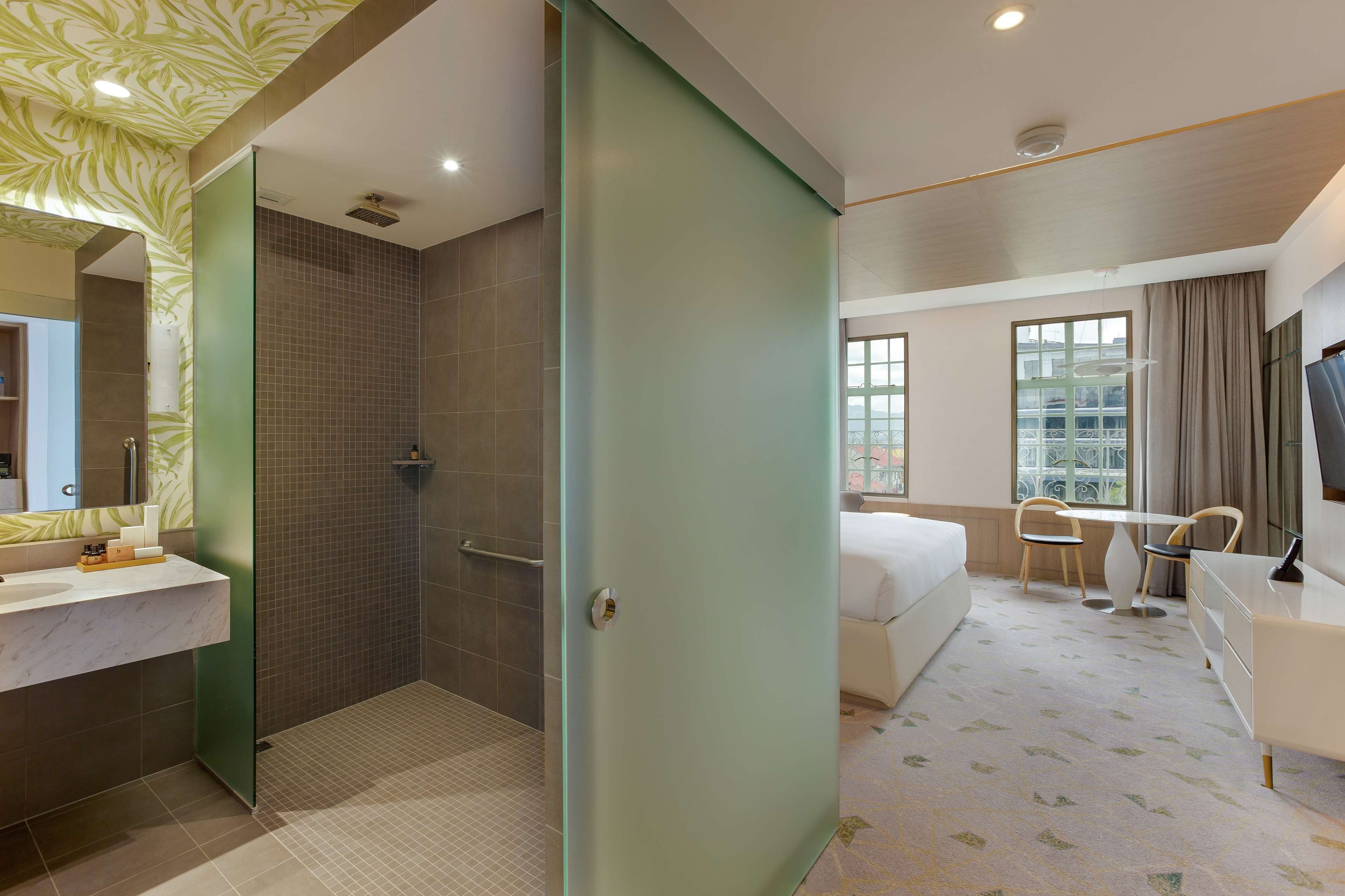 A hotel room with a shower, a bed, a desk, and a chair.