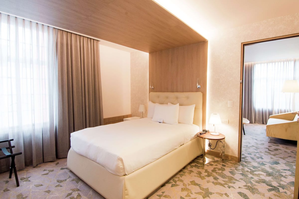 A hotel room with a large bed, a bedside table with a lamp, a chair, and a mirror.