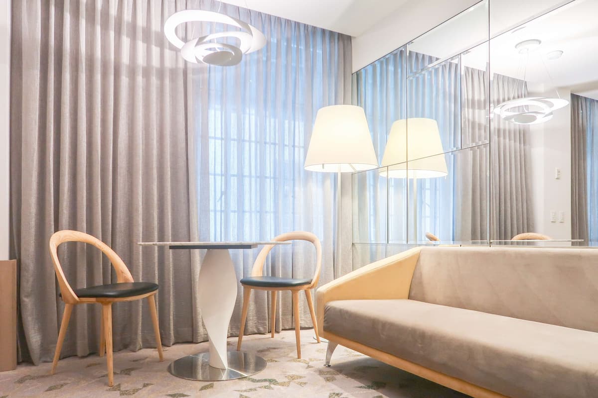 A modern hotel room with a sofa, two chairs, a table, and a large mirror.