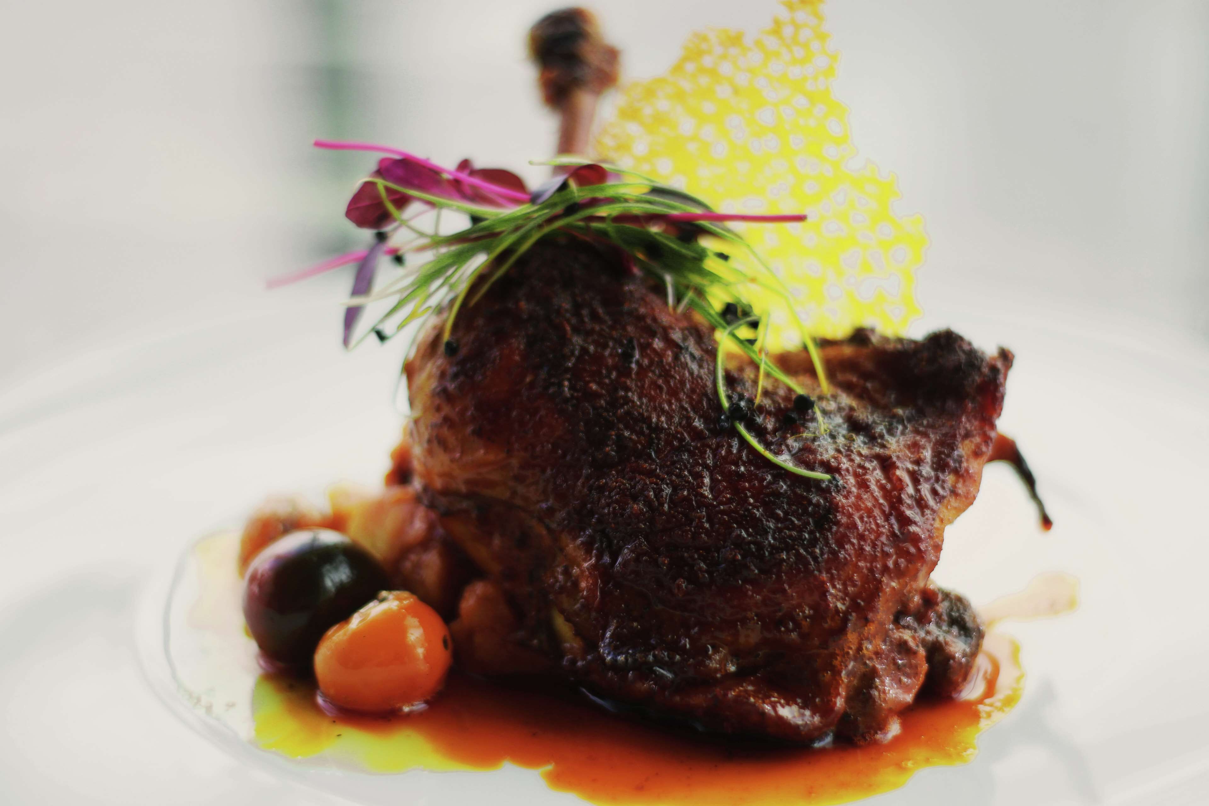 Un plat dont la pièce maîtresse est une viande rôtie, agrémenté d’herbes et d’un élément décoratif, et servi avec des olives et une sauce.