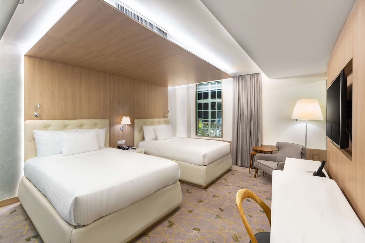 A hotel room with two beds, a desk, a chair, a TV, and a window with curtains.