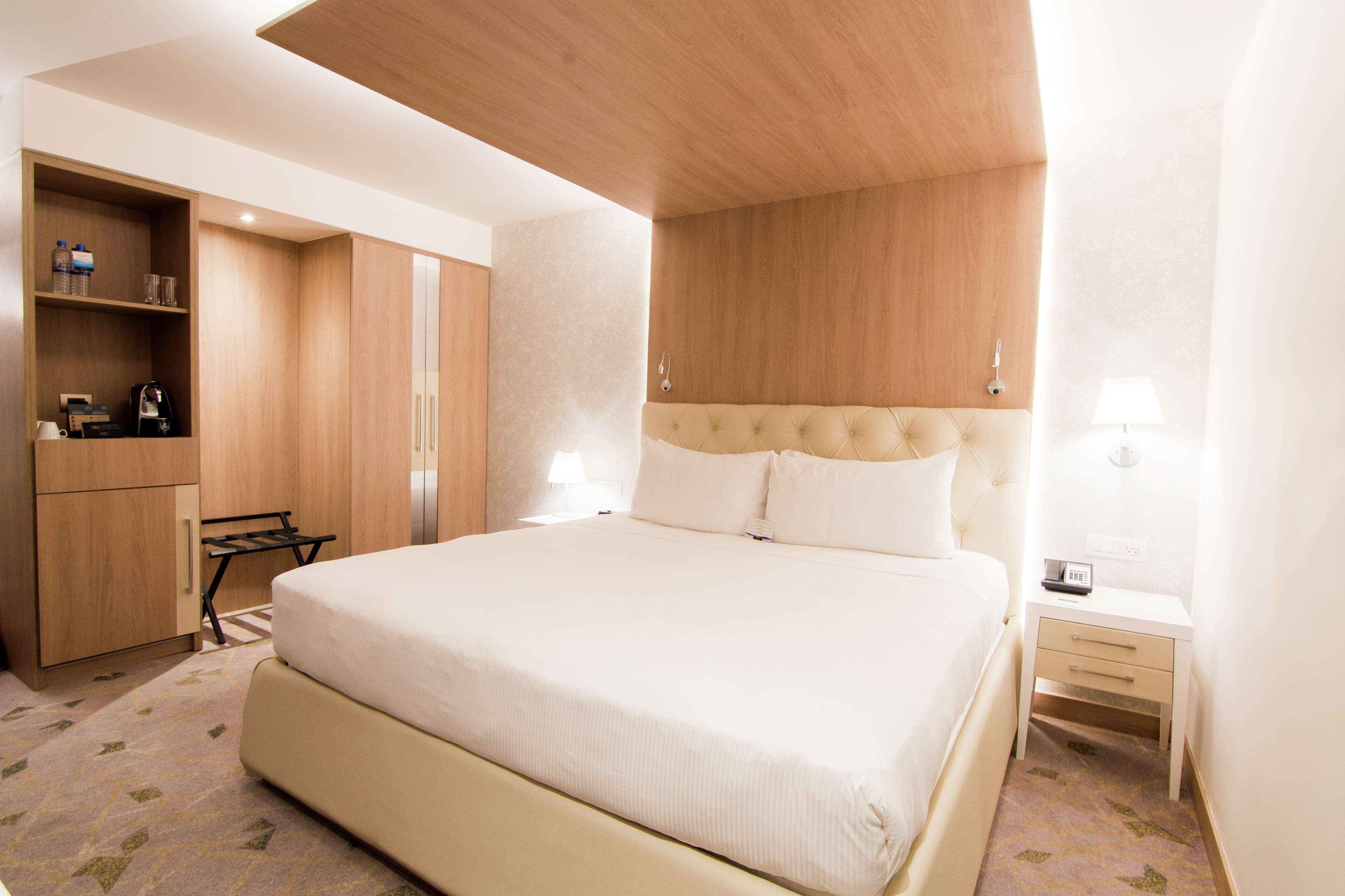 A hotel room with a large bed, a wooden wardrobe, a desk, and a nightstand.