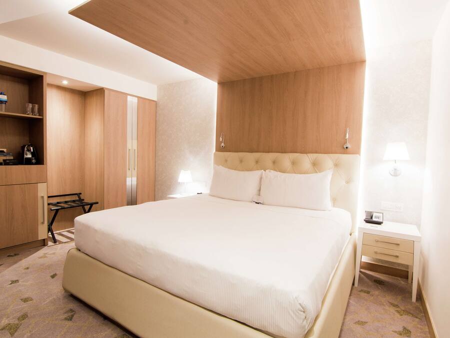 A hotel room with a large bed, a wooden wardrobe, a desk, and a nightstand.
