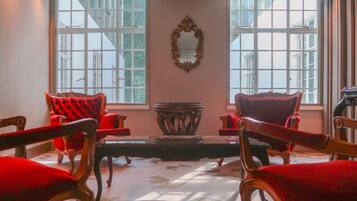 Una habitación con cuatro sillas tapizadas de rojo, una mesa central y un espejo en la pared.