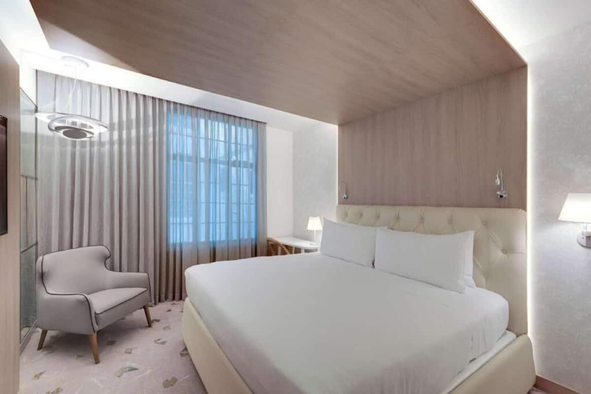 A hotel room with a large bed, a chair, a desk, and a window with curtains.