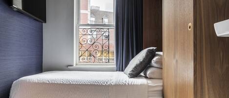 Un dormitorio con cama, ventana con vista a edificios y un armario de madera.