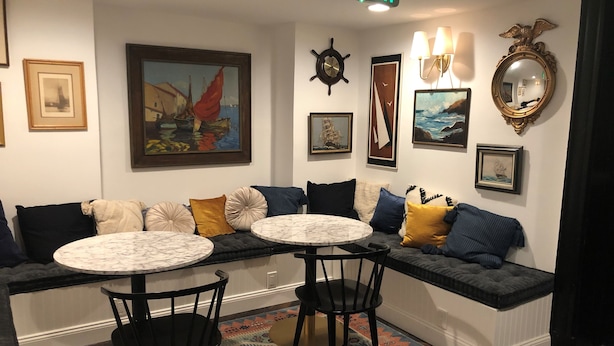 A cozy seating area with a bench, two round tables, and chairs, decorated with cushions and framed artwork on the walls.