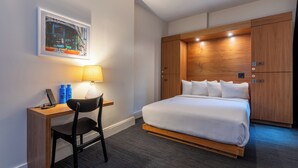 A hotel room with a bed, a desk, a chair, a lamp, and a wardrobe.