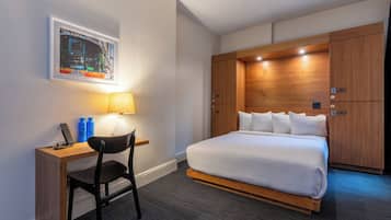 A hotel room with a bed, a desk, a chair, a lamp, and a wardrobe.