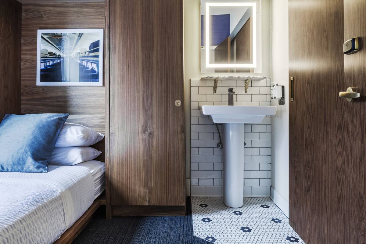 A hotel room with a wooden bed, a white sink, and a tiled floor.