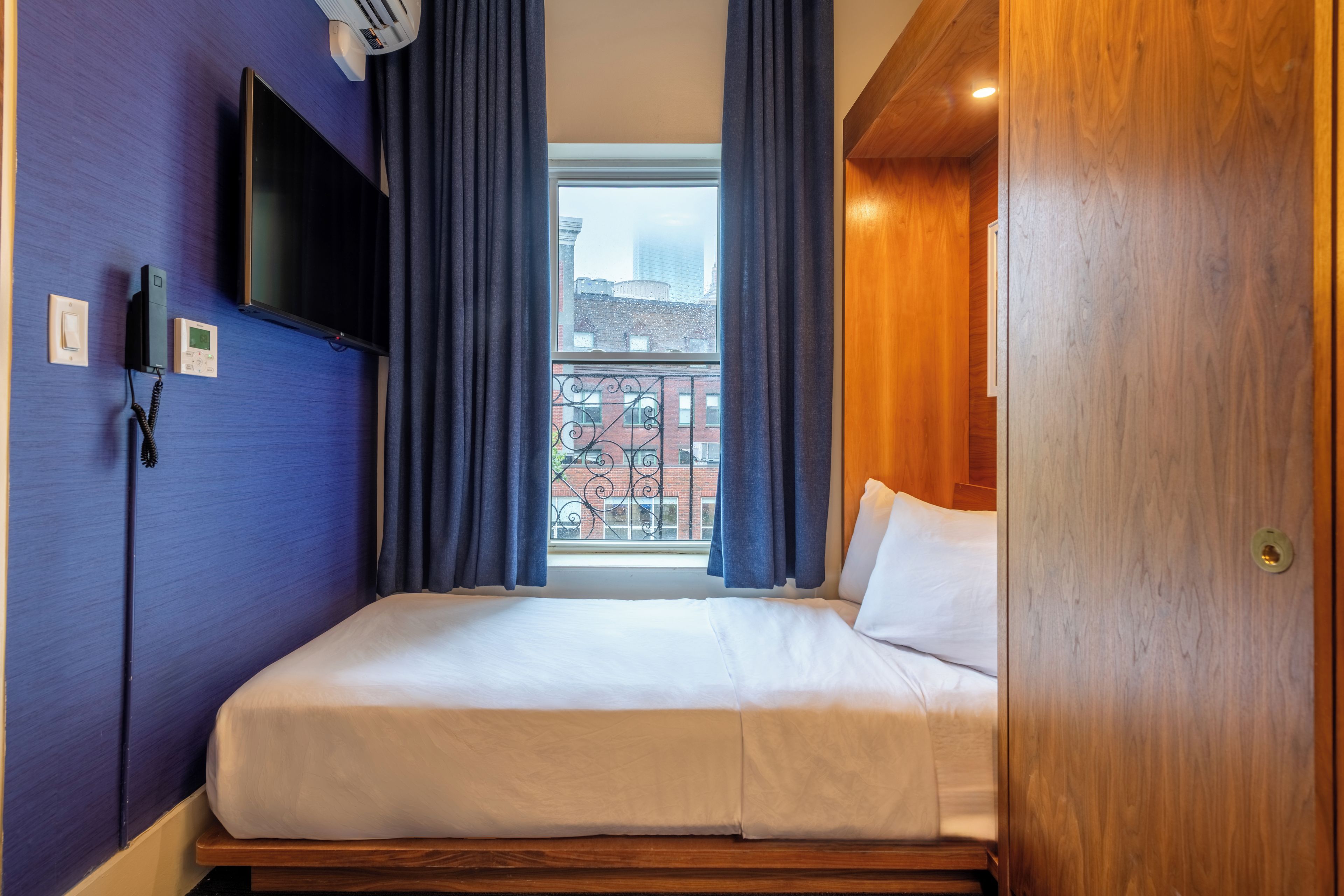 Una habitación de hotel con una cama, un televisor montado en la pared y una ventana con cortinas.