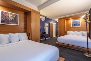 Habitación de hotel con dos camas, un escritorio y una silla. Se observan unidades de aire acondicionado fijadas a la pared y una lámpara.