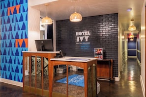 A hotel reception desk with a computer, a wall-mounted sign reading 'HOTEL IVY BOSTON COMMON', and a hallway with a blue carpet leading to a staircase. - Hotel Ivy Boston Common (Boston)