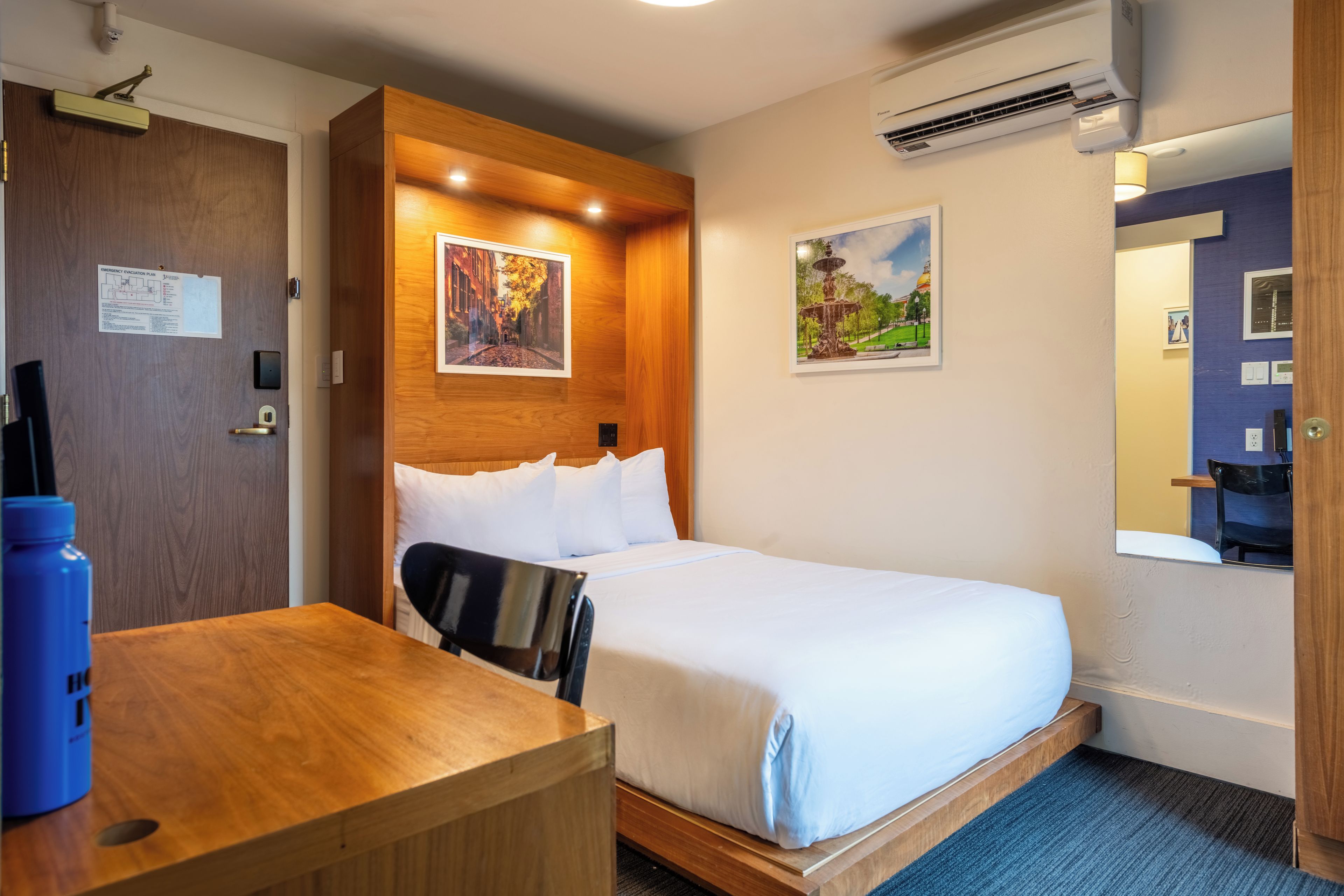 A hotel room with a bed, a desk, and a chair. There are two paintings on the wall.
