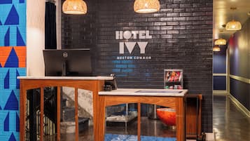Ein Hotelrezeptionstresen mit einem Computer, einem an der Wand befestigten Schild mit der Aufschrift 'HOTEL IV BOSTON COMMON' und einer Treppe, die zu einer oberen Etage führt.